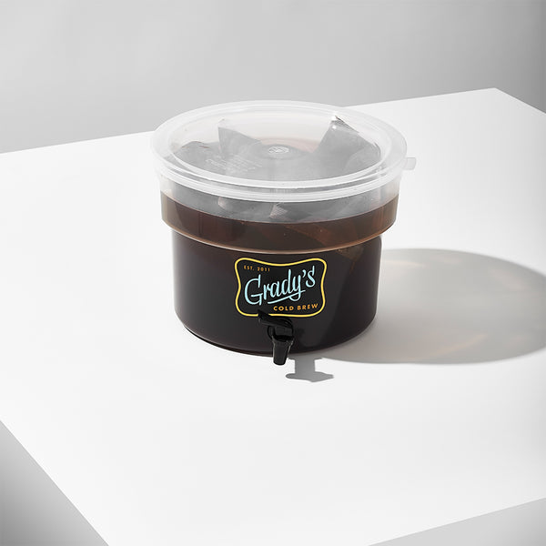 A Grady’s Cold Brew dispenser partially filled with cold brew and visible bean bags steeping inside, sealed with a clear plastic lid.