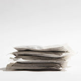 Side view of a stack of five cold brew bean bags made of white compostable filter paper, filled with coffee grounds and resting on a white surface against a light gradient background.