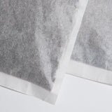 Close-up of two overlapping cold brew bean bags made of white compostable filter paper, showing fine coffee grounds inside and textured sealed edges.