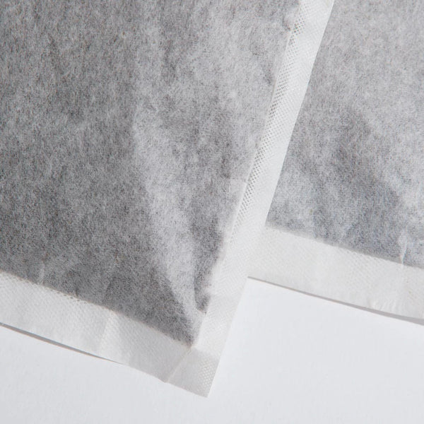Close-up of two overlapping cold brew bean bags made of white compostable filter paper, showing fine coffee grounds inside and textured sealed edges.