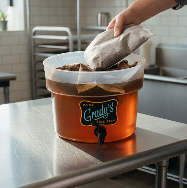 Close-up of a Grady’s dispenser mid steep with submerged bean bags; hand placing one more.
