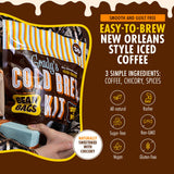 Grady’s Cold Brew Kit pouch resting in someone’s lap like a gift, next to bold text describing it as smooth, guilt free, easy to brew New Orleans style iced coffee made from three ingredients (coffee, chicory, spices) with badges showing it is all natural, kosher, sugar free, non-GMO, vegan, gluten free, and naturally sweetened with chicory.