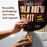 Hands pour iced cold brew from the tap of a Grady’s Cold Brew Kit pouch into a glass of ice, with text reading “Reusable packaging: Just rinse and repeat!